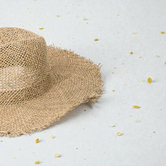 Beige straw hat on a light gray surface with scattered yellow seeds.