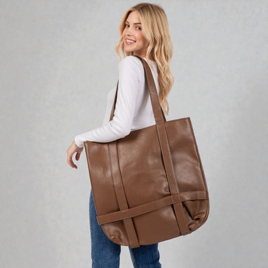 Woman carrying a brown leather tote bag against a plain background
