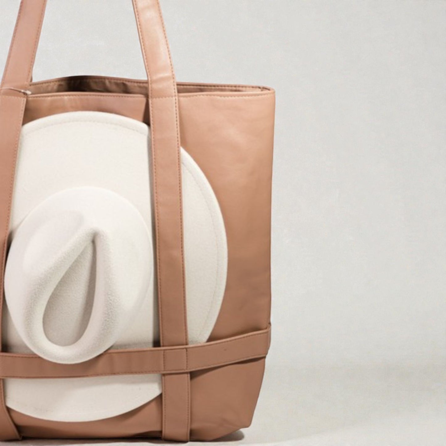 Brown tote bag with a white rolled-up blanket inside on a light gray background