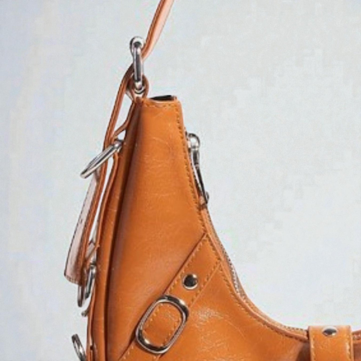 Close-up of a brown leather handbag with metal hardware on a light gray background
