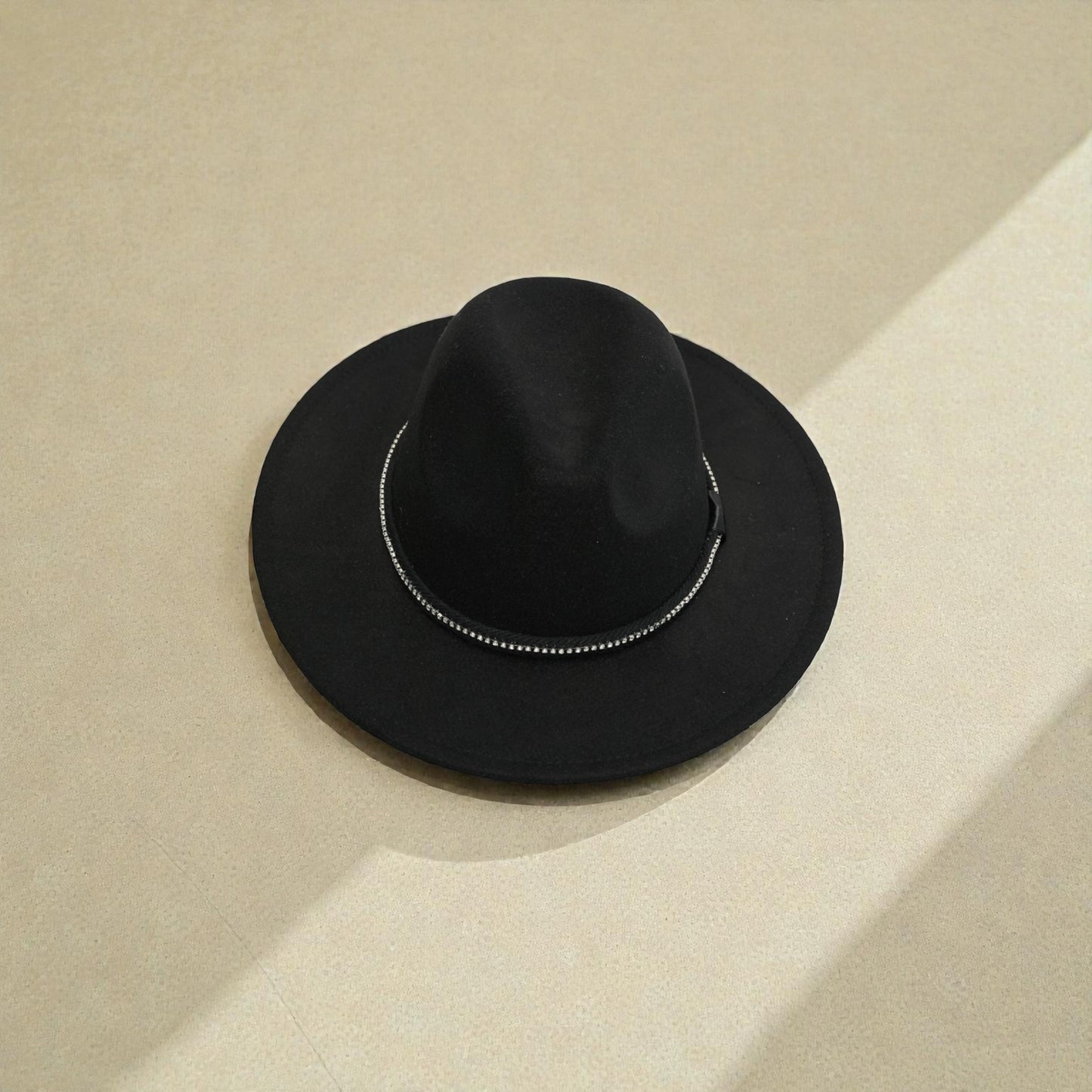 Black fedora hat with a decorative band on a beige background