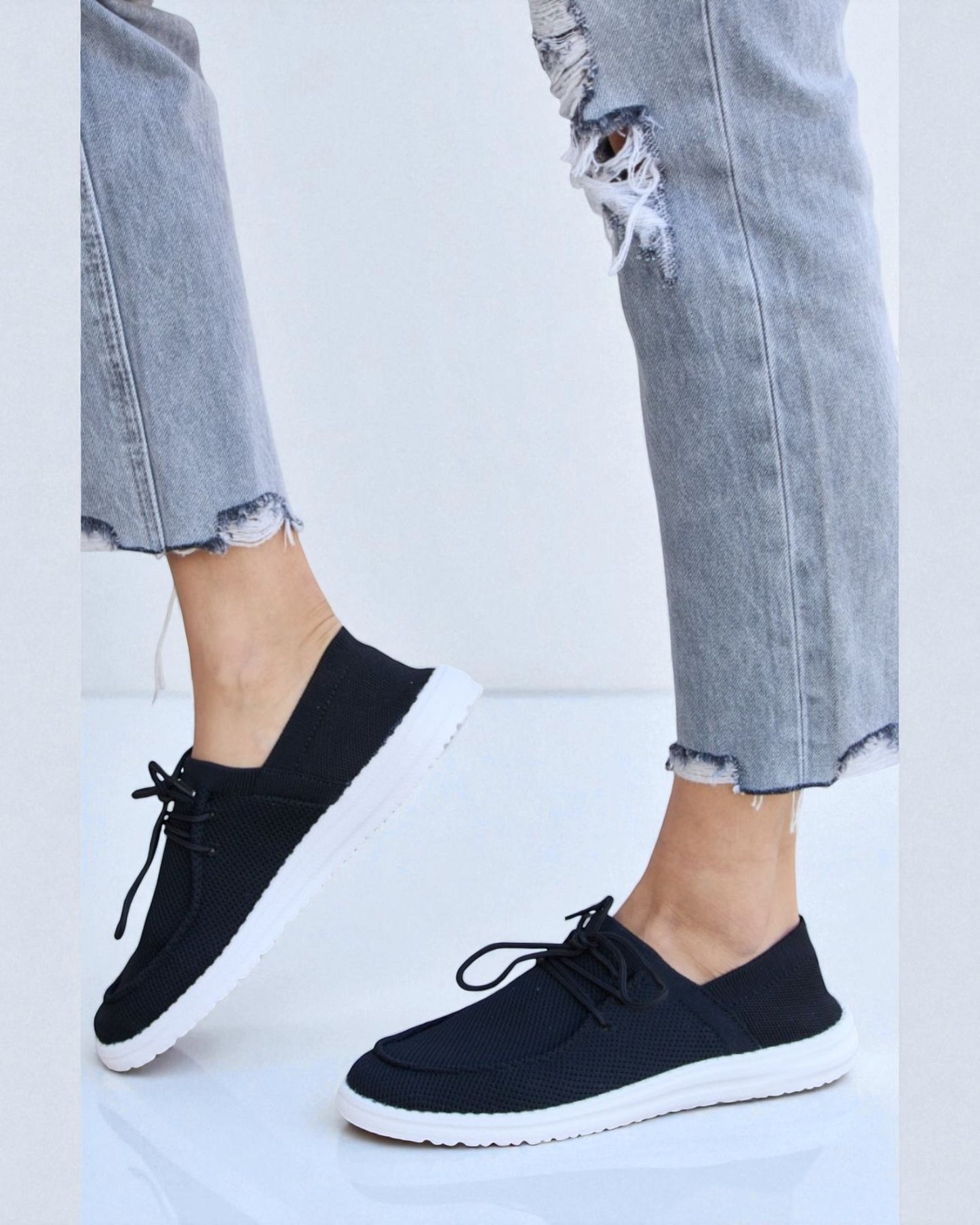 Black sneakers worn with ripped jeans on a white background