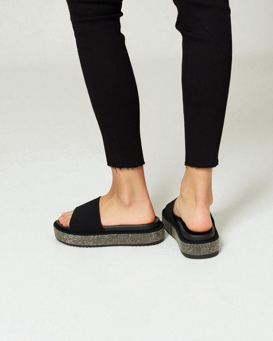 Black sandals worn with black pants on a white background