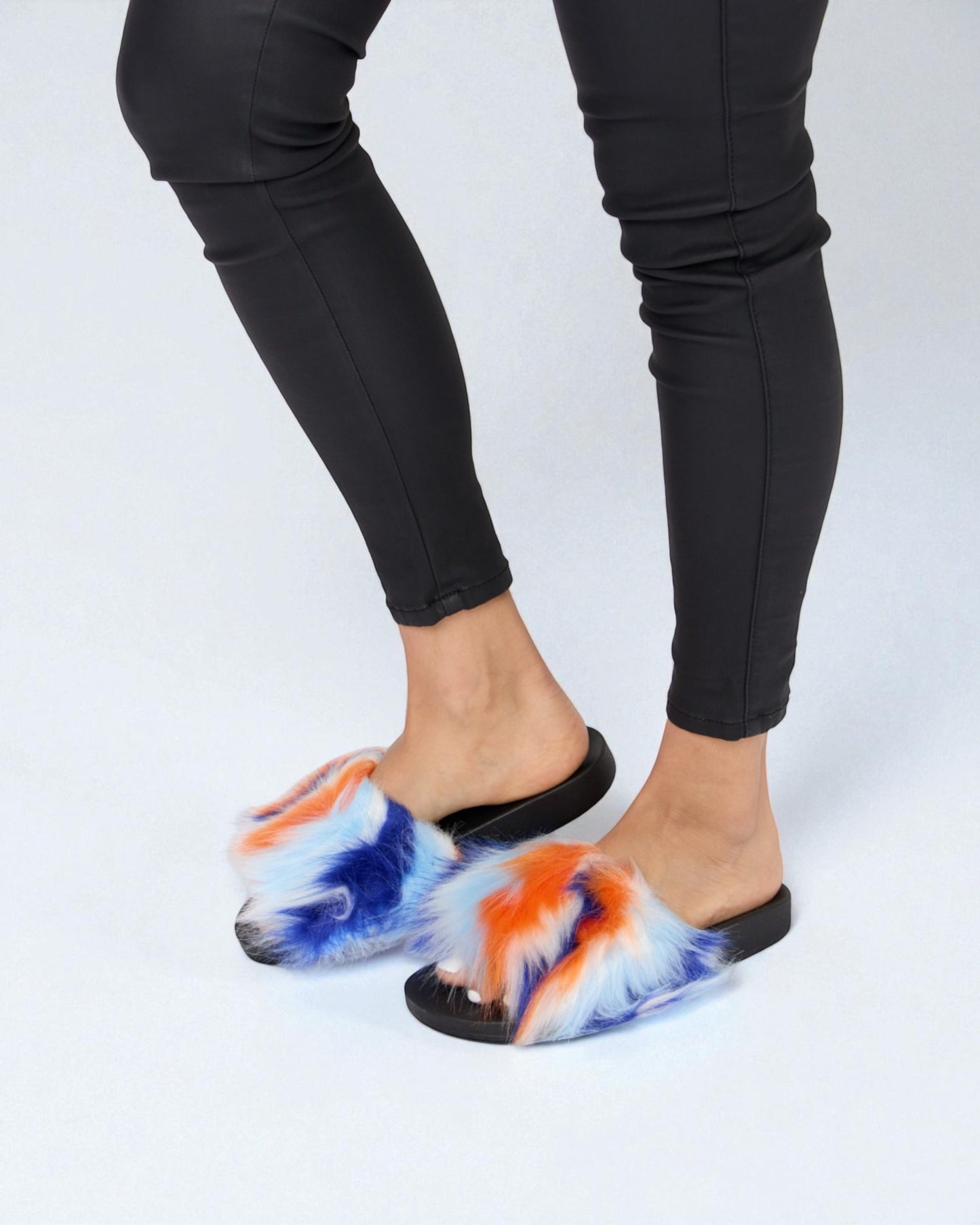 Person wearing tie-dye slippers with black pants on a white background