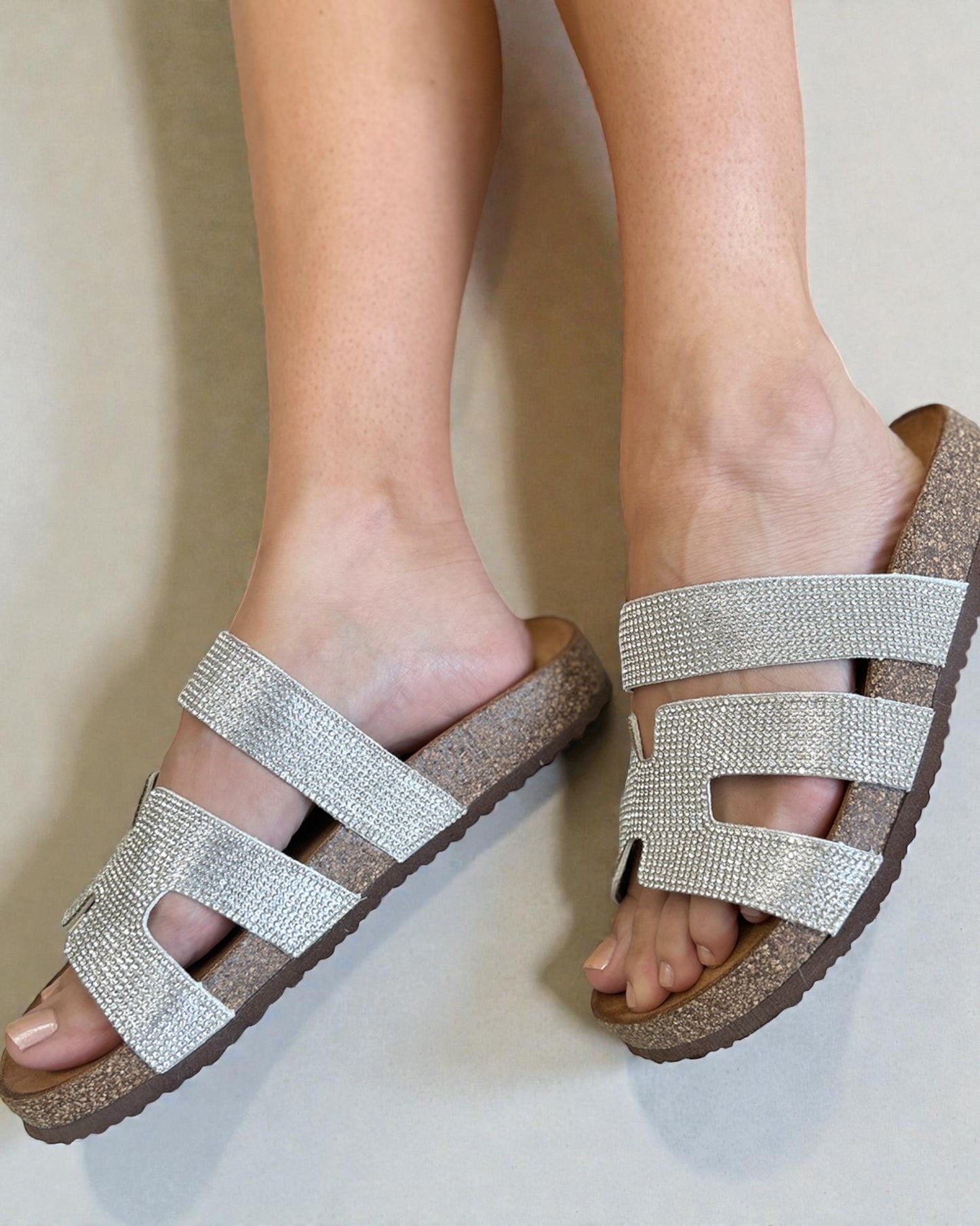 Silver strappy sandals on feet against a neutral background