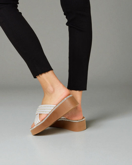 Brown sandal with a platform worn by a person in black pants on a gray background