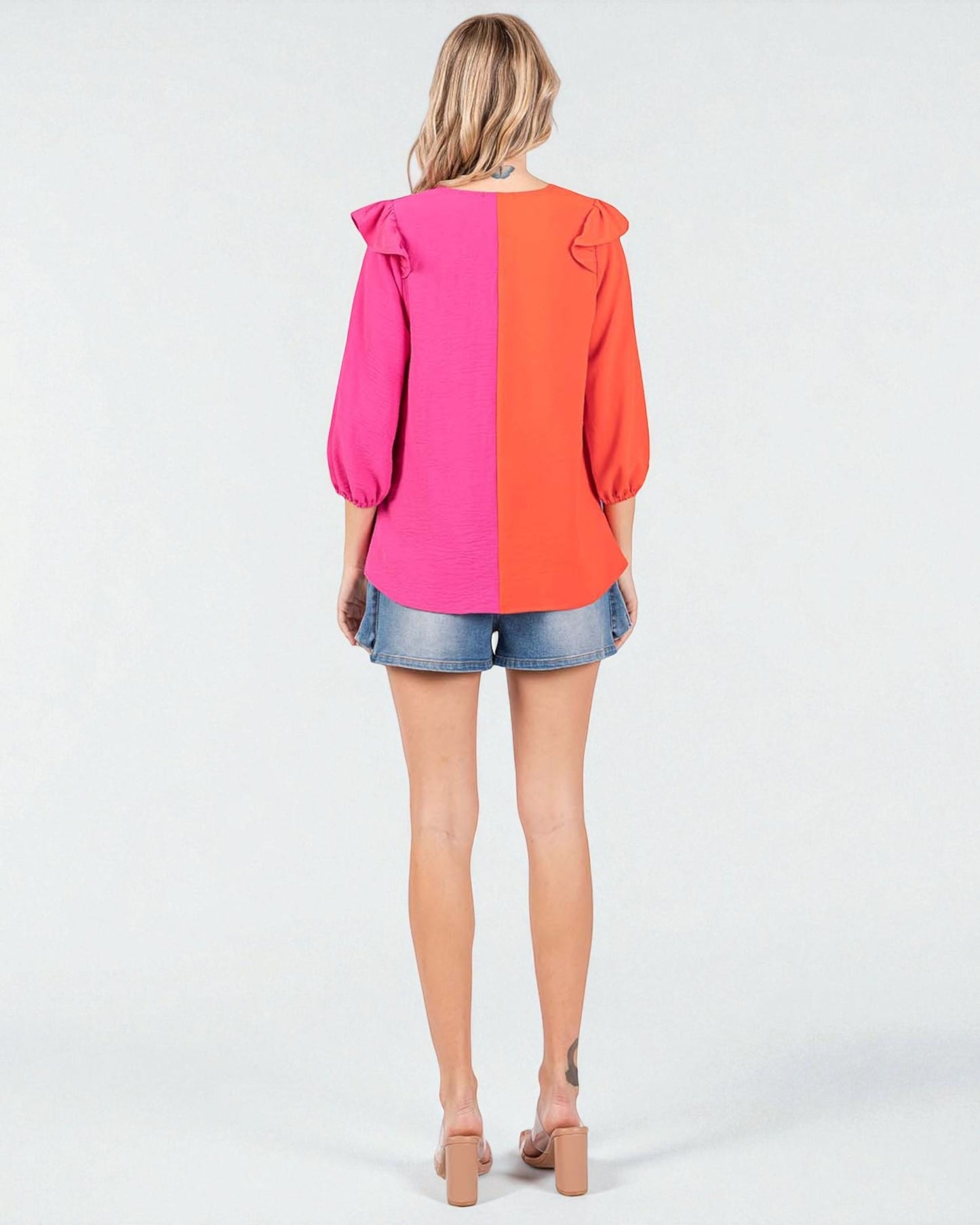 Woman wearing a two-tone pink and orange blouse with denim shorts on a white background