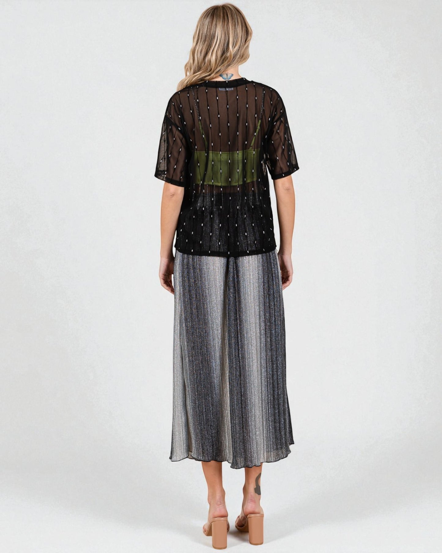 Woman wearing a black top with sheer sleeves and a long silver skirt on a white background