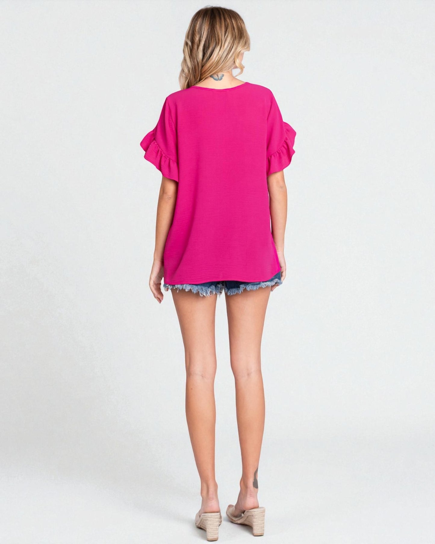 Woman wearing a bright pink top and denim shorts on a white background
