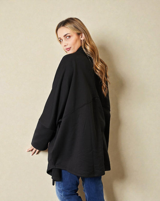 Woman wearing a black coat and blue jeans against a beige wall