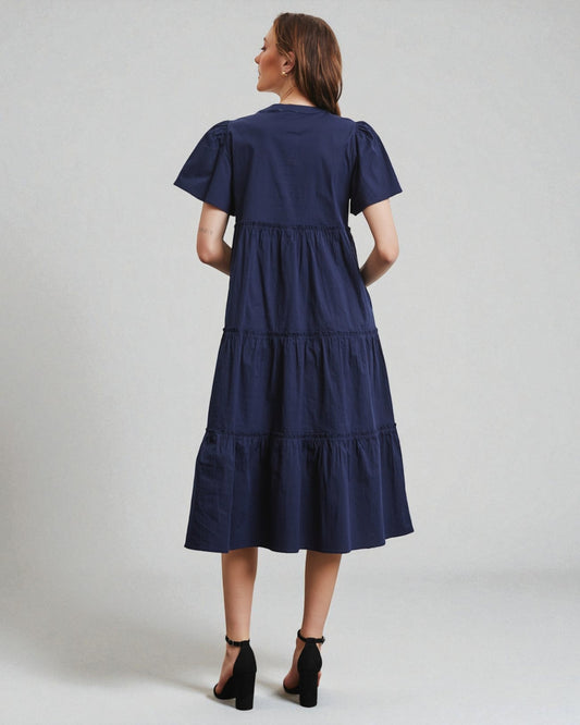 Woman wearing a navy blue dress with ruffled sleeves on a light gray background