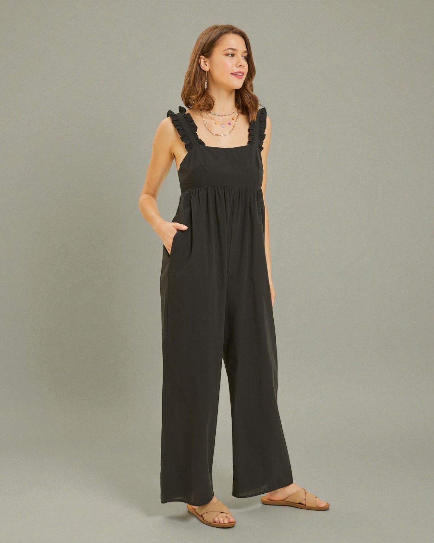 Woman wearing a black jumpsuit with ruffled straps on a gray background