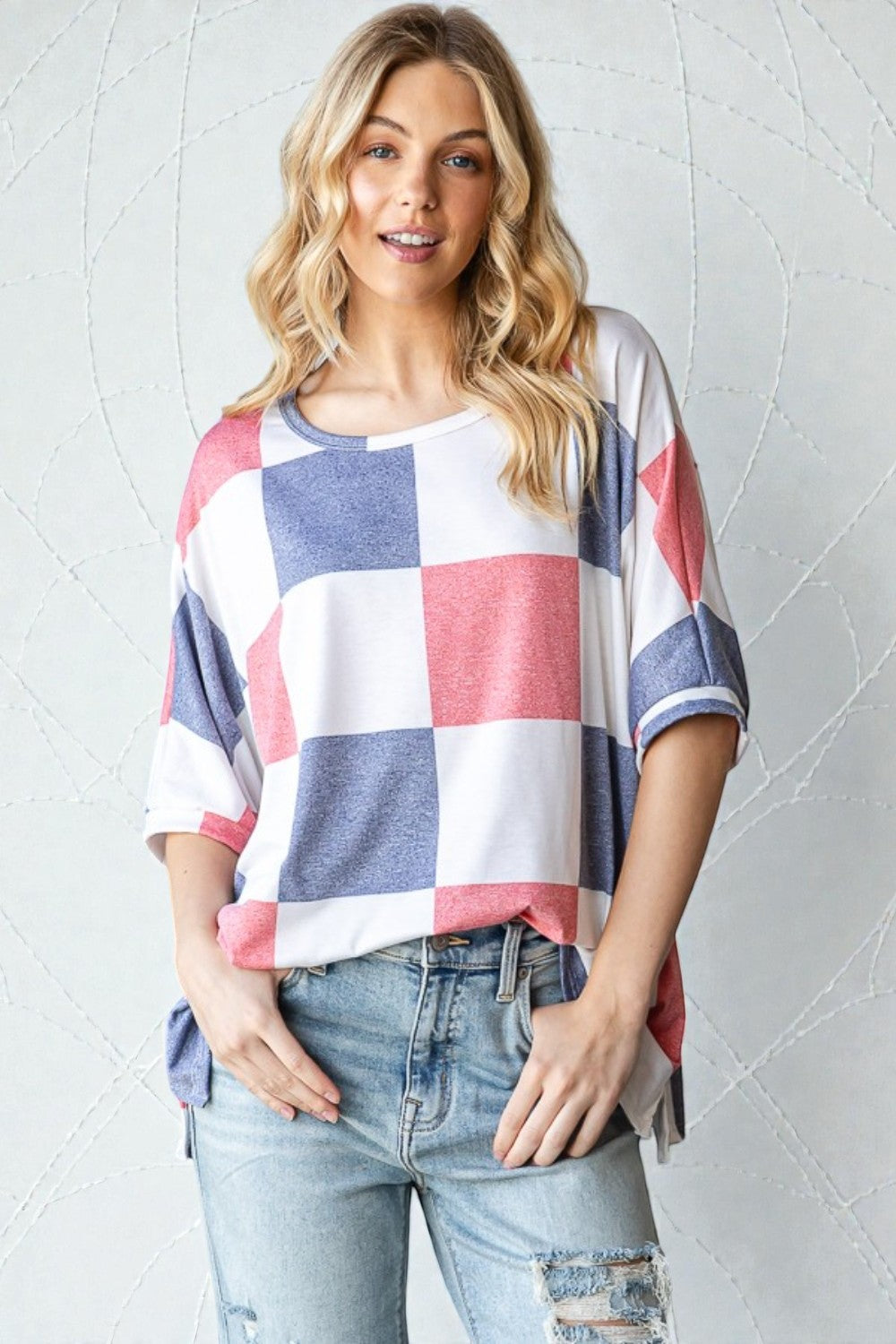Woman wearing a checkered top with red, white, and blue colors against a light gray background.