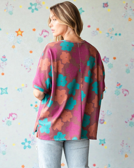 Woman wearing a colorful floral-patterned sweater against a patterned wall.