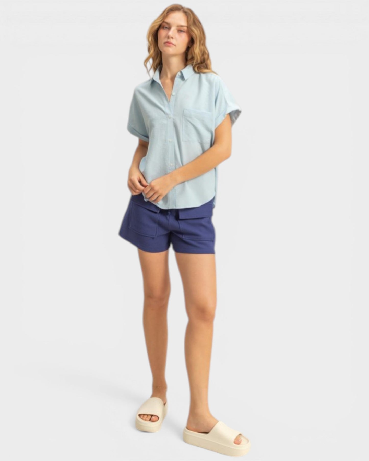 Woman wearing a light blue shirt and blue shorts on a white background
