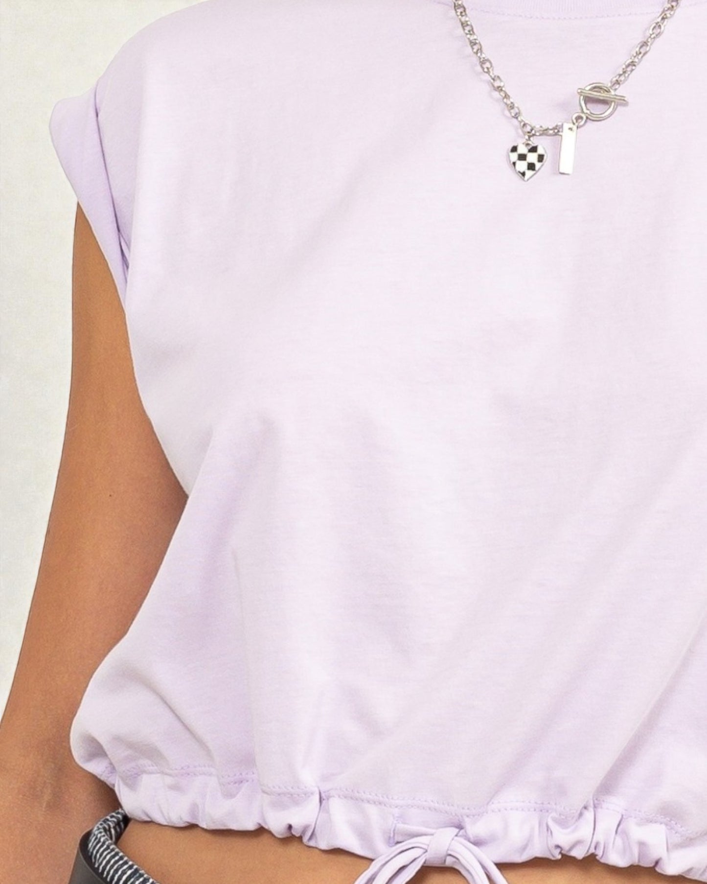 Close-up of a person wearing a light purple top with a necklace featuring a small bag charm.
