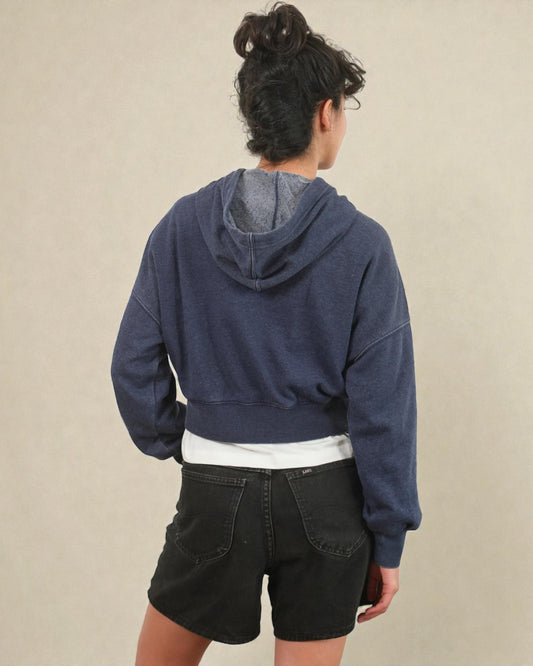 Person wearing a blue hoodie and black shorts on a beige background