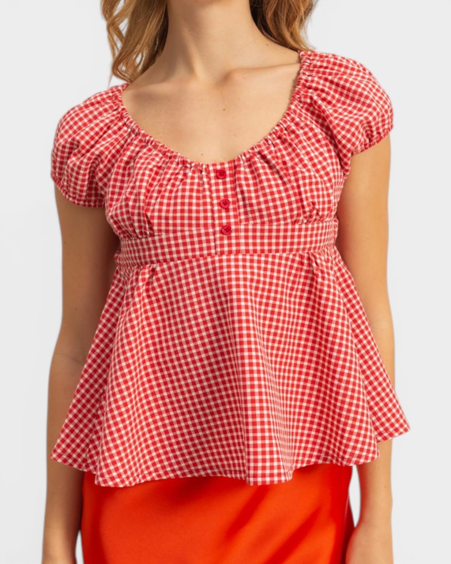 Red and white checkered top worn by a person on a plain background