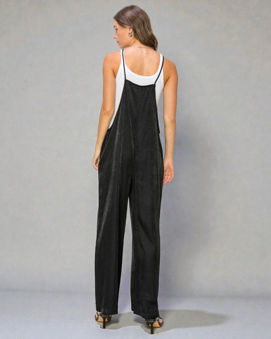 Woman wearing a black overalls with a white top against a gray background