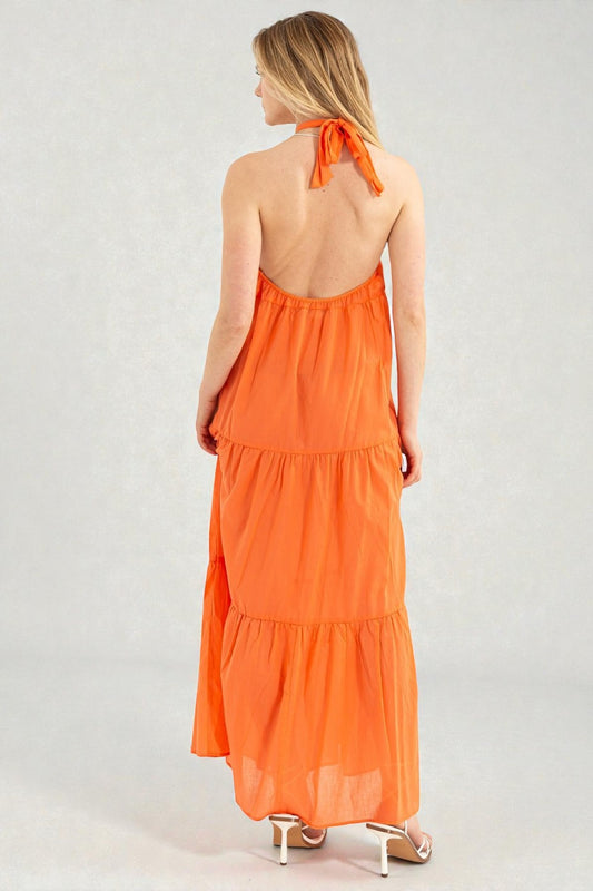 Woman wearing an orange halter neck dress on a plain background