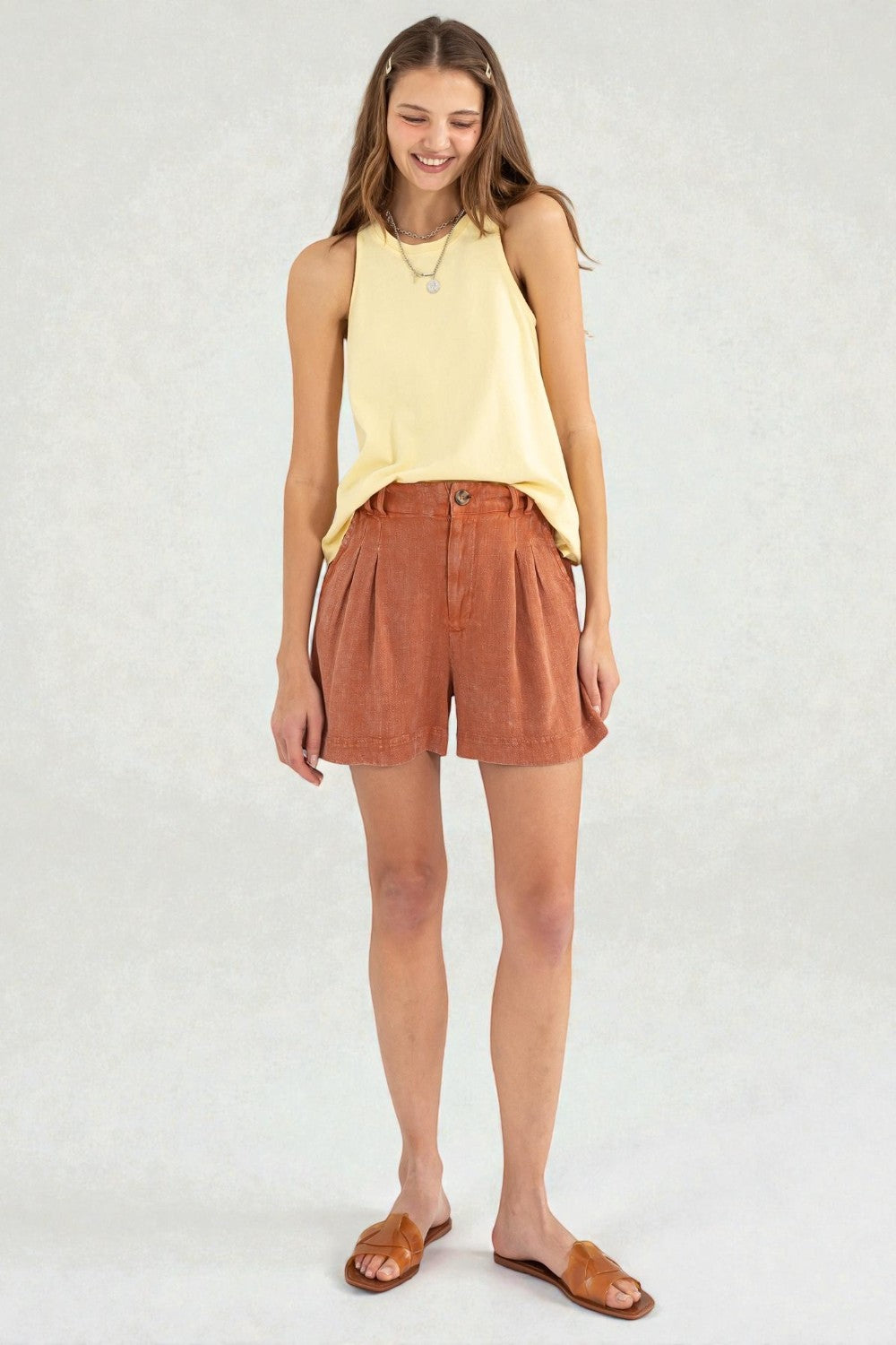 Woman wearing a yellow sleeveless top and brown shorts on a white background