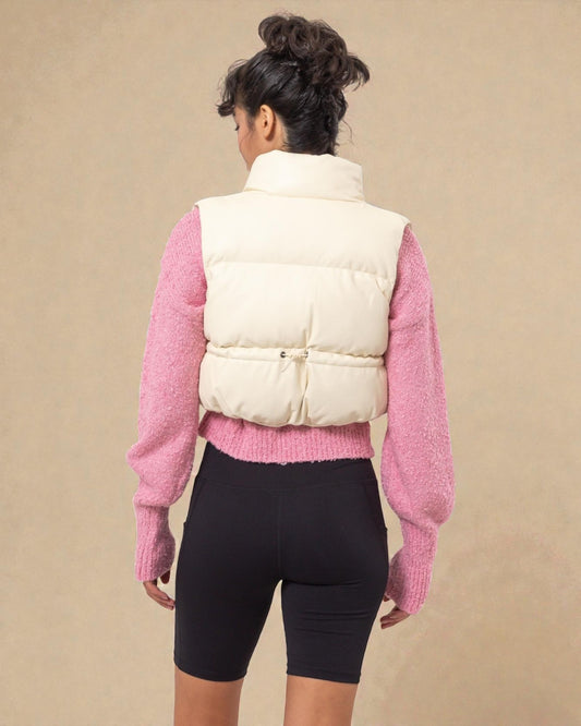Person wearing a white puffer vest over a pink sweater on a beige background