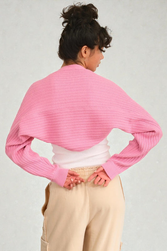 Person wearing a pink ribbed sweater over a white top and beige pants on a light gray background