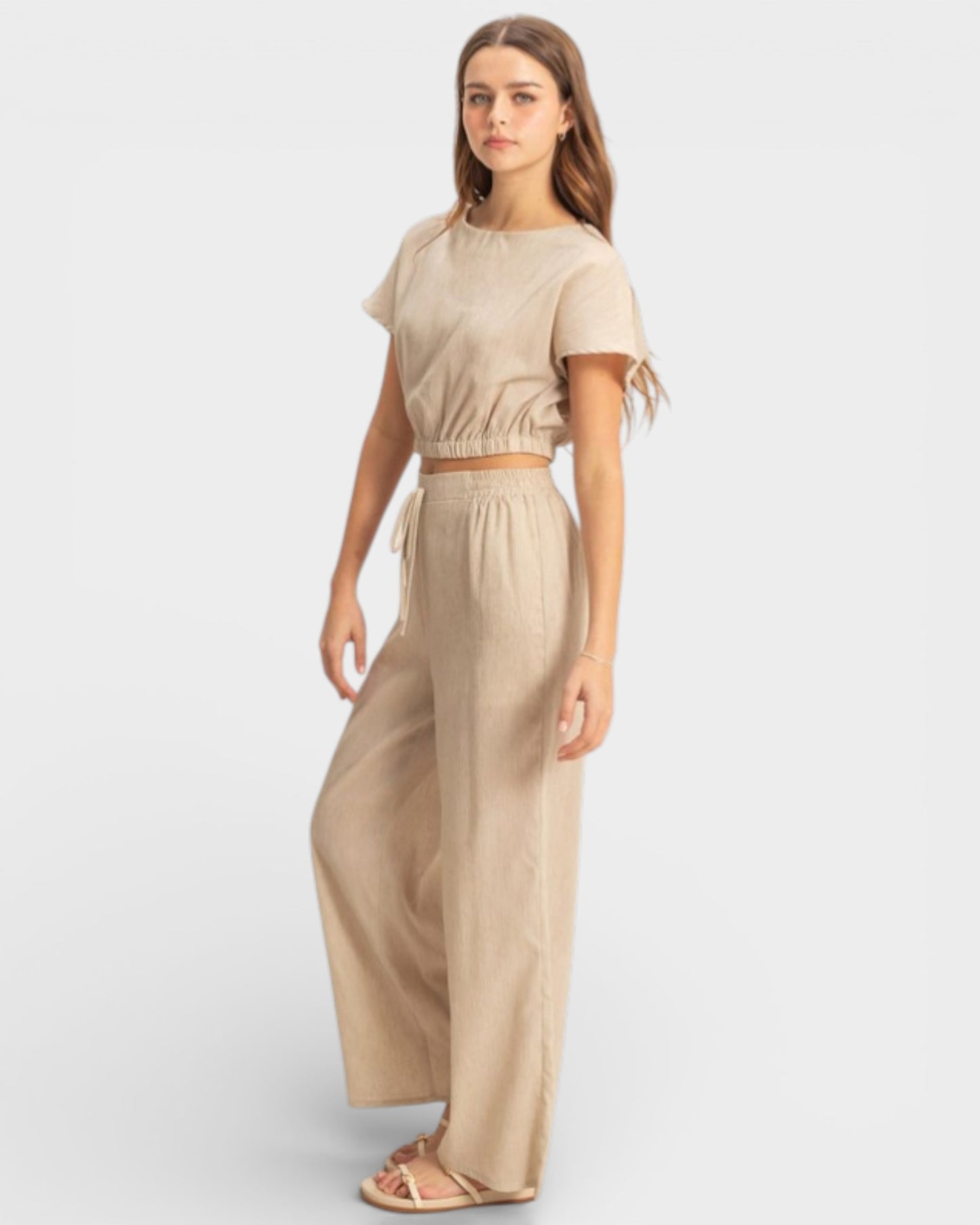 Woman wearing a beige outfit with wide-leg pants on a white background