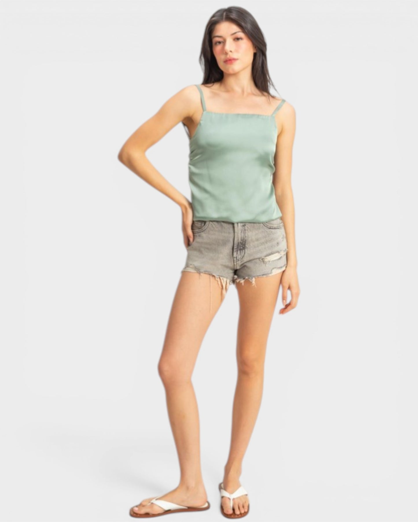 Woman wearing a light green tank top and denim shorts on a white background