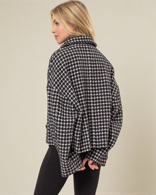 Woman wearing a black and white houndstooth patterned shirt against a plain background