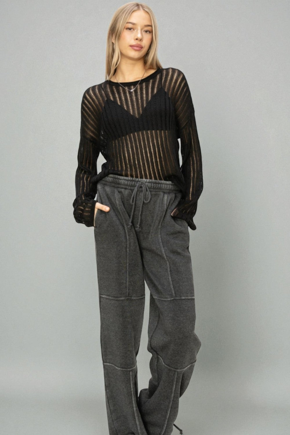 Person wearing a black sheer top and gray pants on a plain background