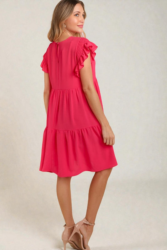 Woman wearing a pink dress with ruffled sleeves on a plain background