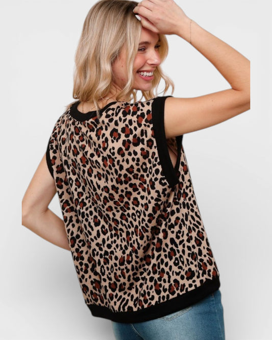 Woman wearing a leopard print top with black trim on a plain background