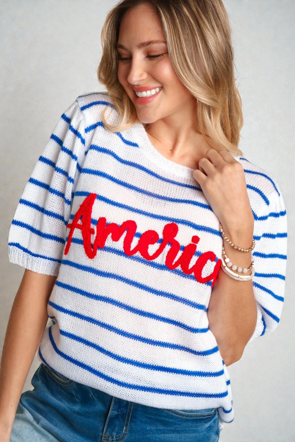 Woman wearing a white and blue striped sweater with 'America' printed on it against a gray background