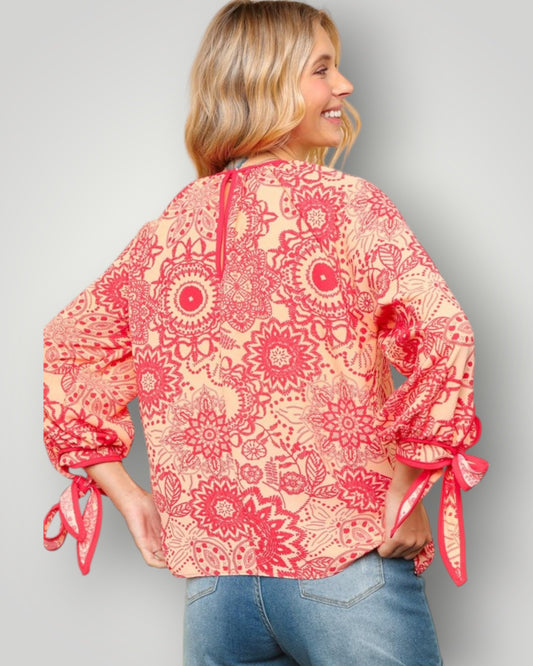 Woman wearing a red floral blouse with tied sleeves on a gray background