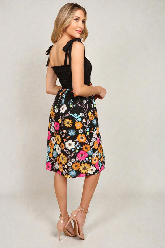 Woman wearing a black top and colorful floral skirt on a plain background