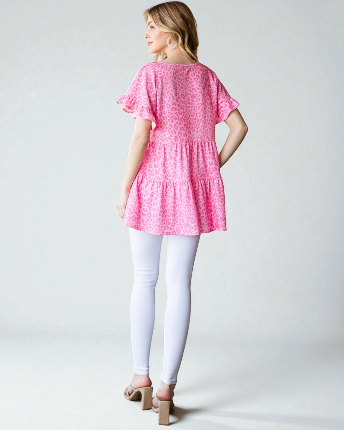 Woman wearing a pink floral dress and white leggings on a plain background