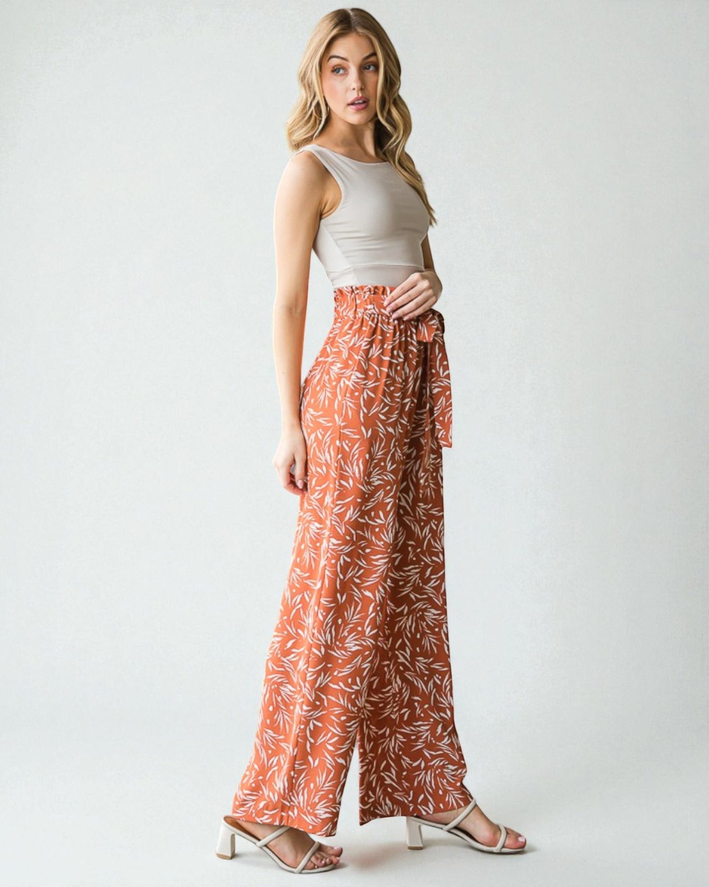 Woman wearing a white top and orange patterned pants on a white background