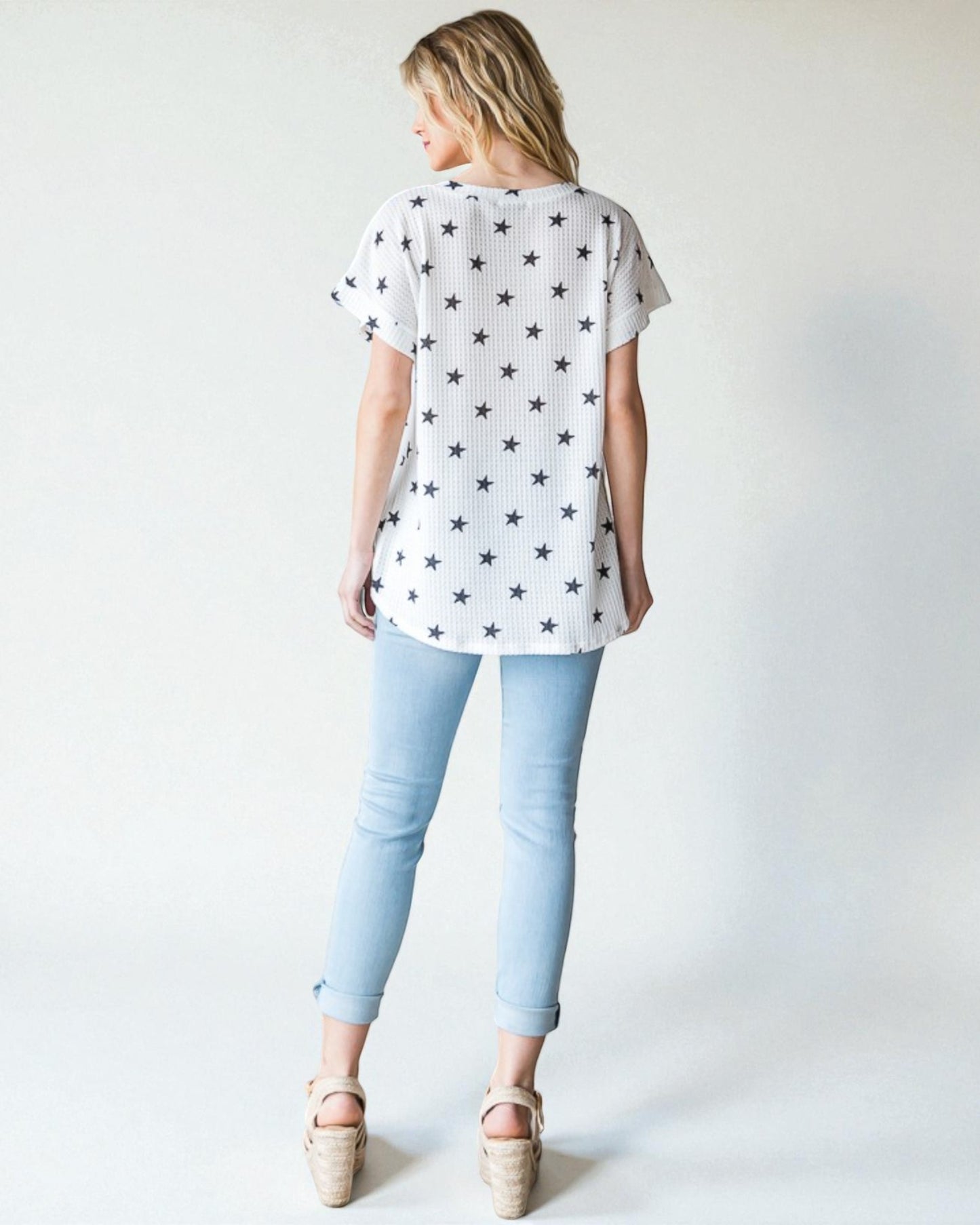 Woman wearing a white t-shirt with star pattern and light blue jeans on a plain background