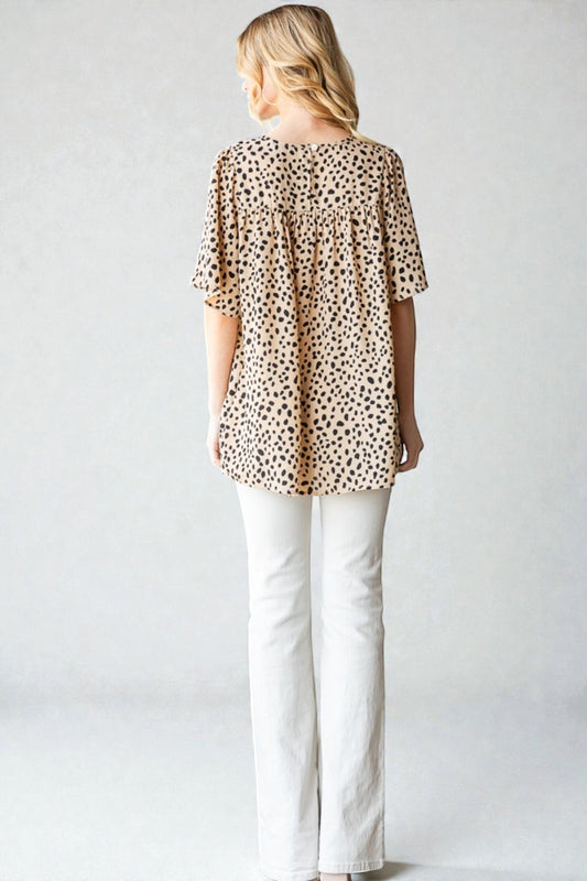 Woman wearing a leopard print top and white pants against a plain background