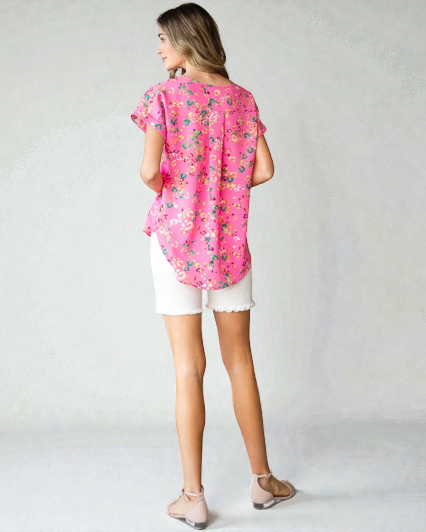 Woman wearing a pink floral blouse and white shorts on a plain background