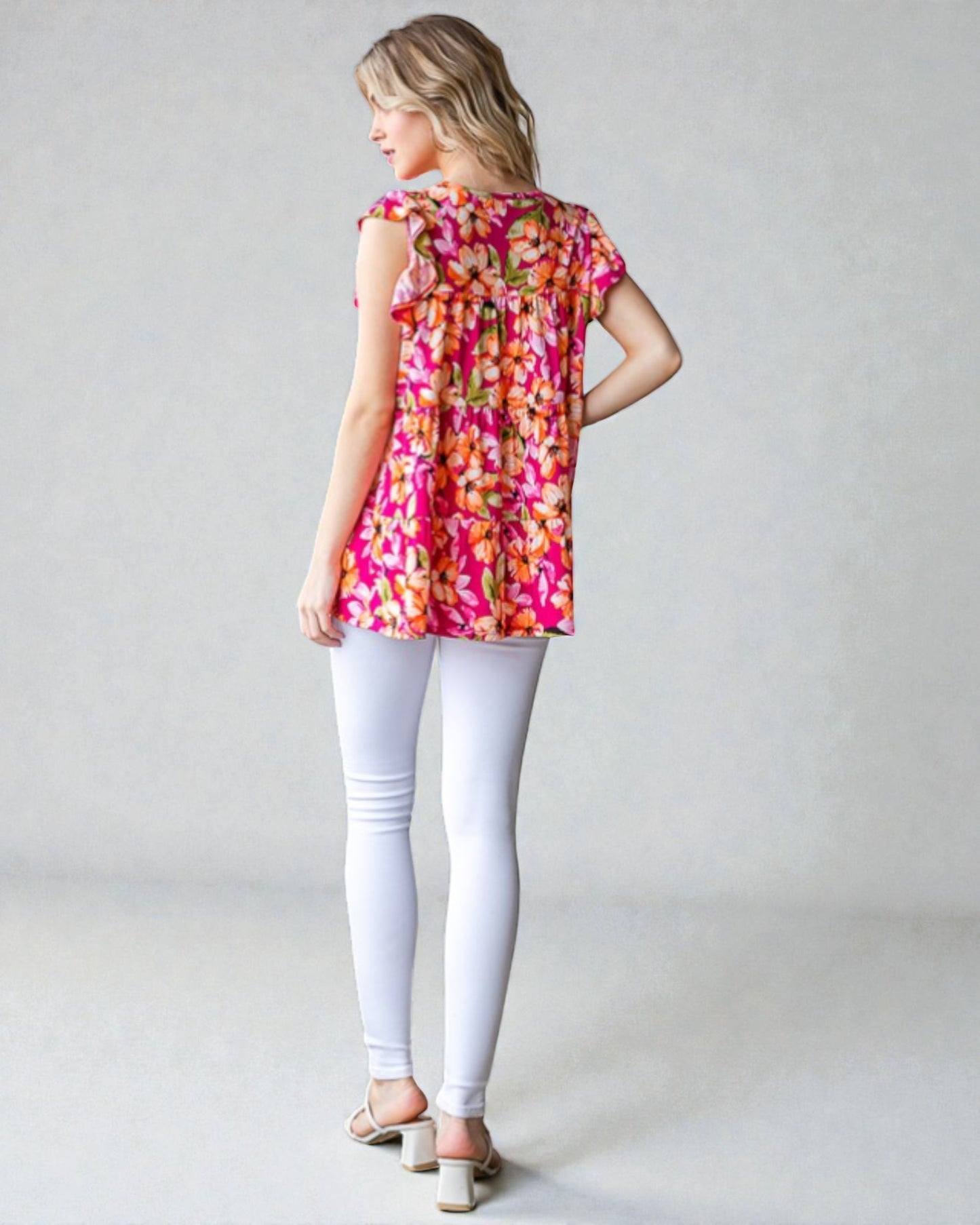 Woman wearing a colorful floral top and white pants on a plain background