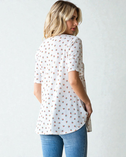 Woman wearing a white blouse with a subtle pattern and blue jeans against a plain background
