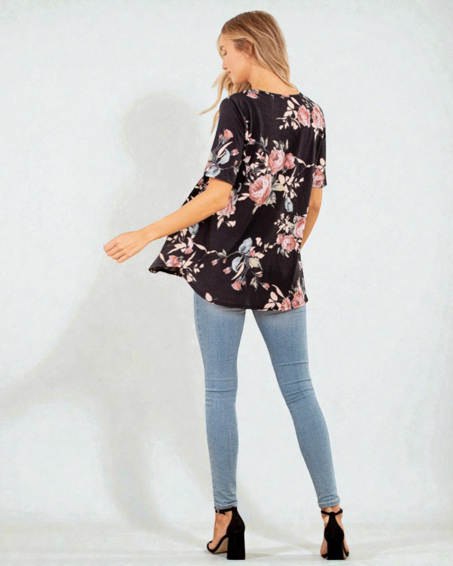 Woman wearing a black floral blouse and light blue jeans on a white background