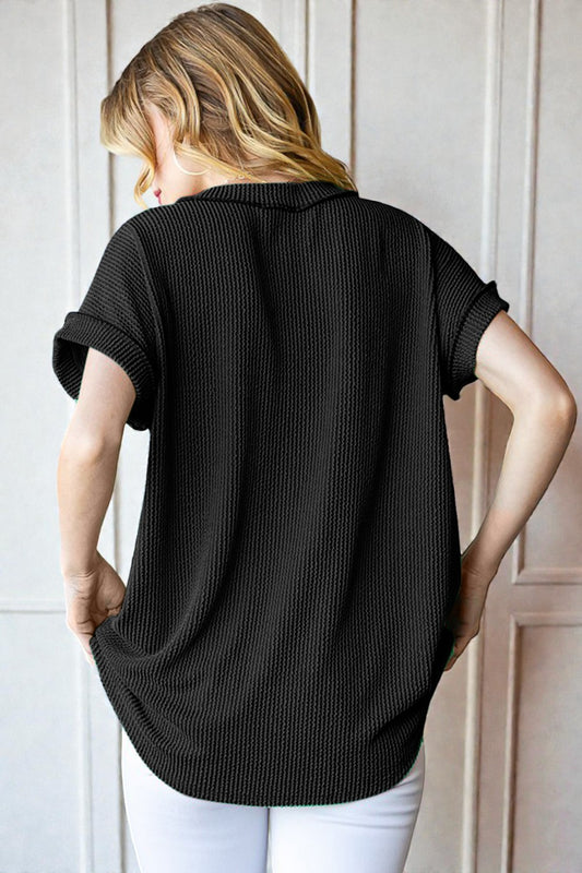 Woman wearing a black ribbed knit shirt against a white paneled wall.
