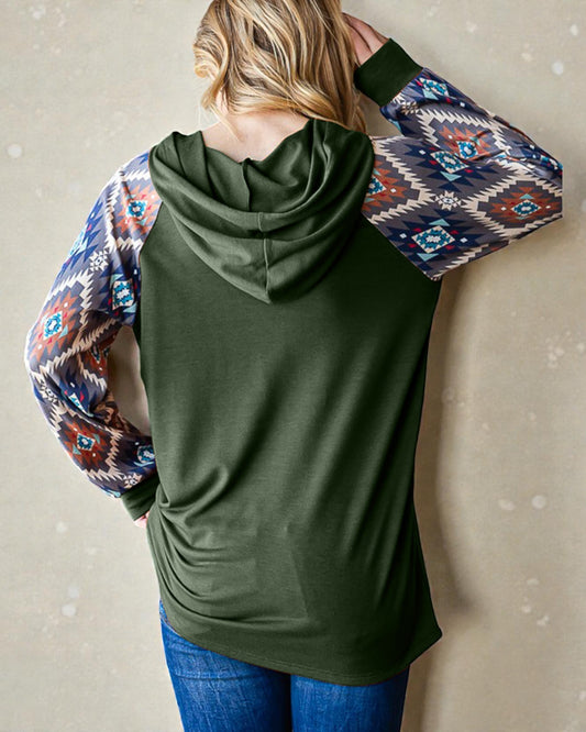 Green hoodie with patterned sleeves worn by a person against a beige wall.
