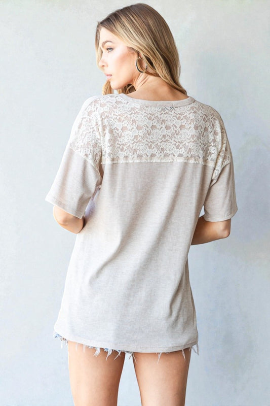 Woman wearing a beige t-shirt with lace detailing on a plain background