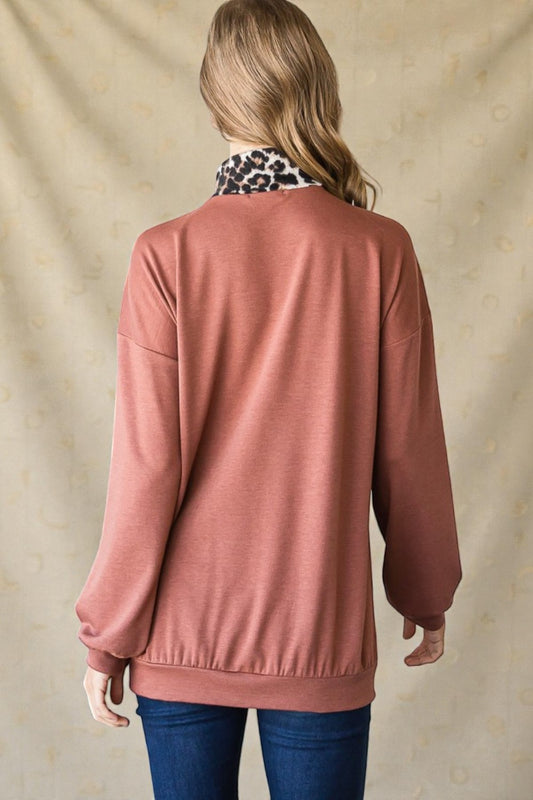 Person wearing a brown sweater with a leopard print scarf, standing against a beige background