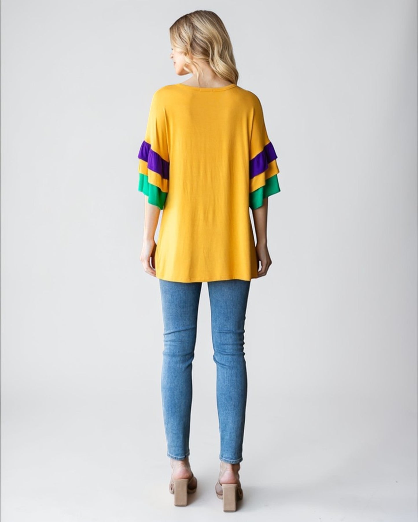 Woman wearing a yellow sweater with colorful sleeves and blue jeans on a white background