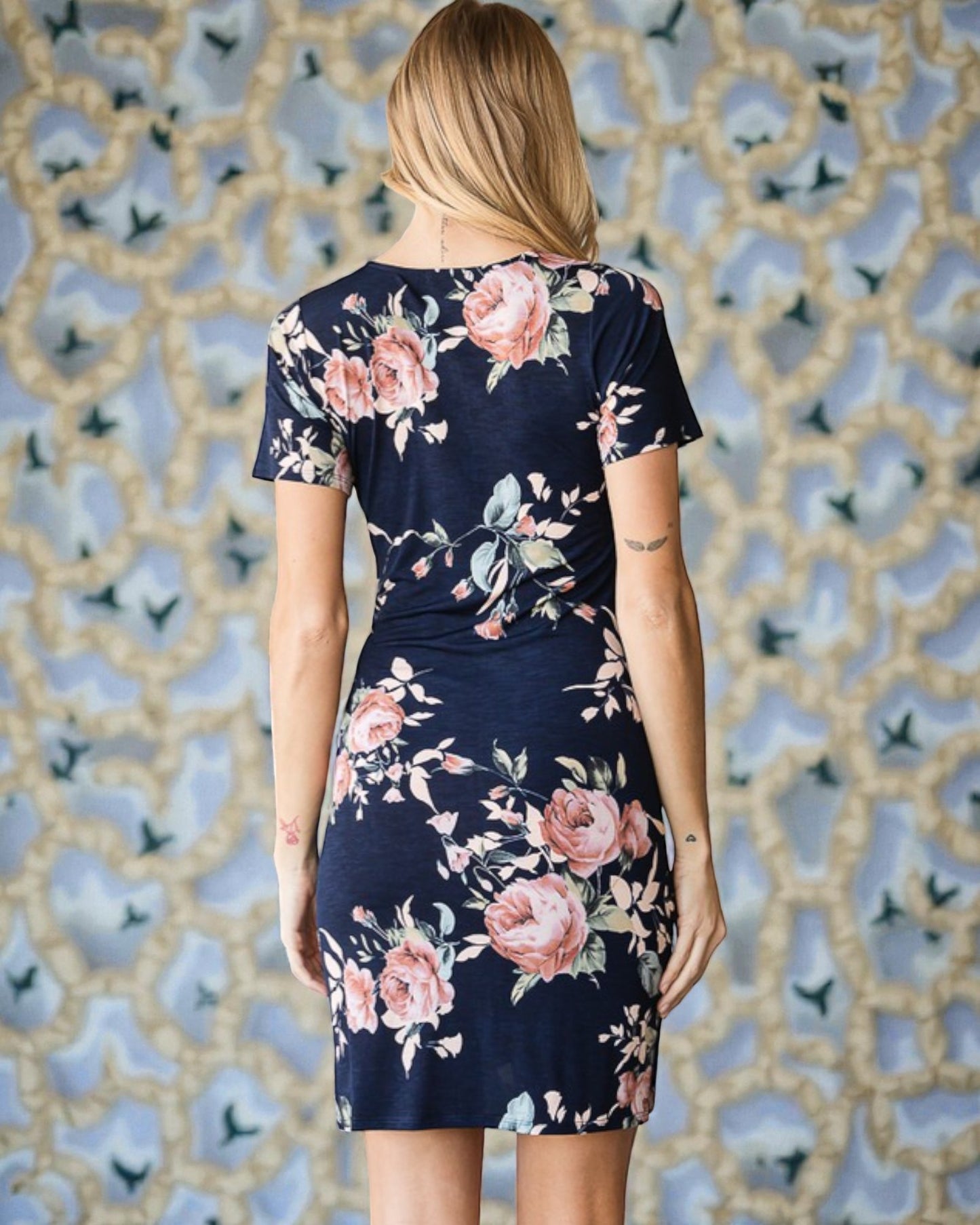 Woman wearing a navy floral dress against a decorative wall.
